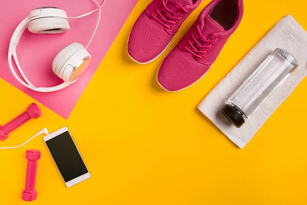 Fitness-Accessoires auf gelbem Hintergrund. Turnschuhe, Wasserflasche, Kopfhörer und Hanteln. — Stockfoto