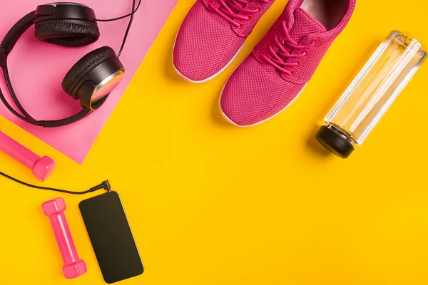 Fitness-Accessoires auf gelbem Hintergrund. Turnschuhe, Wasserflasche, Kopfhörer und Smart. — Stockfoto