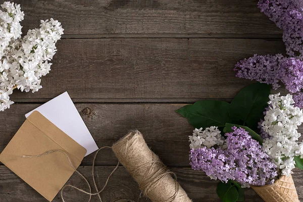 Lilac blossom on rustic wooden background with empty space for greeting message. Scissors, thread reel, small envelope. Top view