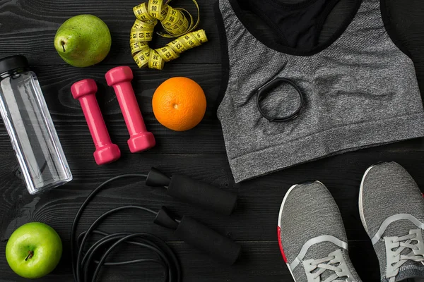 Athletes set with female clothing, sneakers and bottle of water on dark background