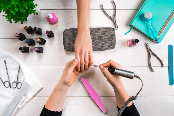 Manicure for the client. Close-up of the hands of a manicurist and client on a wooden background