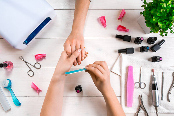 Manicure for the client. Close-up of the hands of a manicurist and client on a wooden background