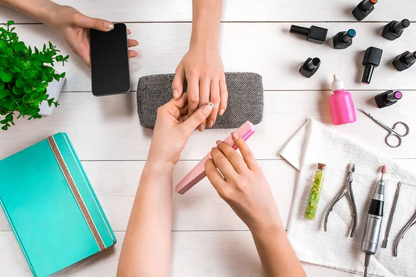 Manicure para o cliente. Close-up das mãos de uma manicure e cliente em um fundo de madeira — Fotografia de Stock