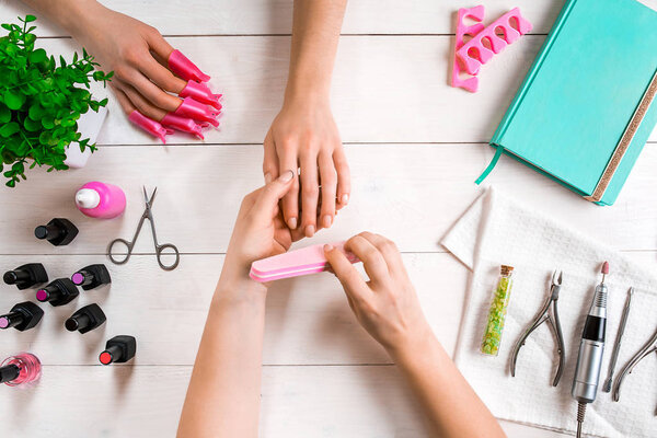 Manicure for the client. Close-up of the hands of a manicurist and client on a wooden background