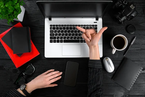 Business and technology topic: the hand of woman in a black shirt showing gesture against background laptop at the desk. — Stock Photo, Image