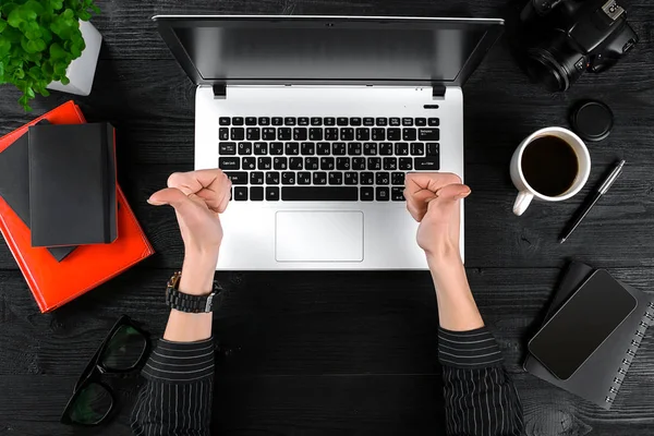 Woman working at the office table. Top view of human hands, laptop keyboard, a cup of coffee, smartphone, notebook and a flower on a wooden table background