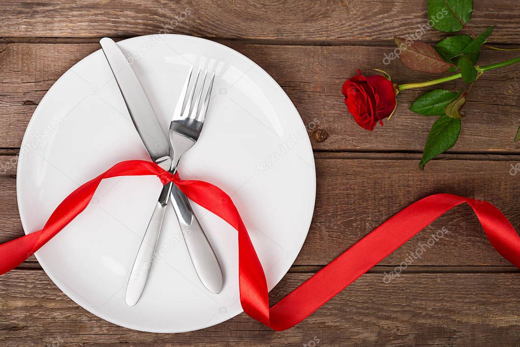 Valentines day table setting with plate, fork, knife, ribbon and rose.   background