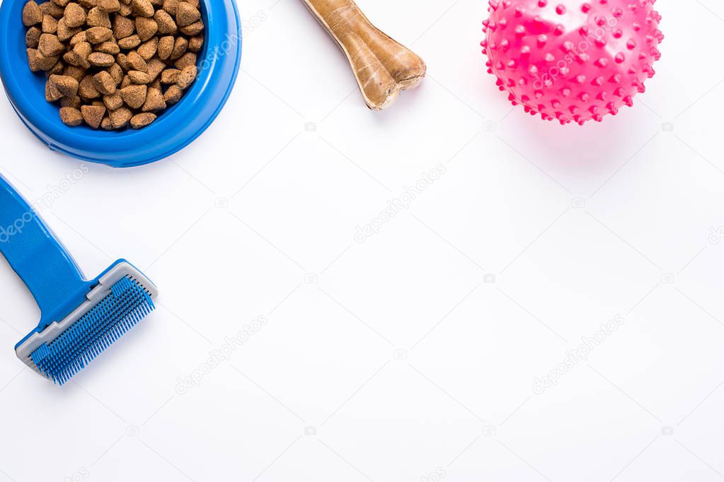 dry pet food in bowl and toys for dogs on white background top view