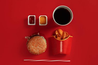 Fast food yemek üstten görünüm. Et burger, patates cipsi ve bardak içki kırmızı zemin üzerine. Paket servisi olan restoran kompozisyon.