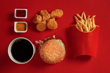 Hamburger, patates, sos, tavuk nuggets ve içki kırmızı zemin üzerine sahte kavramı. Kopya alanı için metin ve logosu.