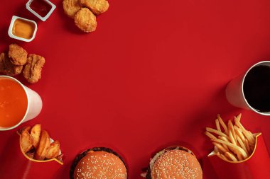 Fast food yemek üstten görünüm. Et burger, patates cipsi ve bardak içki kırmızı zemin üzerine. Paket servisi olan restoran kompozisyon.