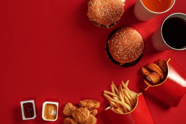 Fast food yemek üstten görünüm. Et burger, patates cipsi ve bardak içki kırmızı zemin üzerine. Paket servisi olan restoran kompozisyon.