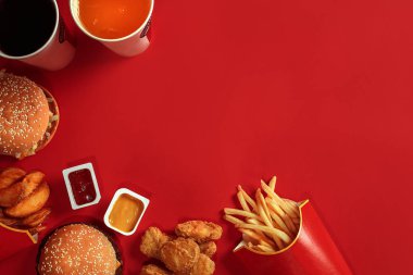 Fast food yemek üstten görünüm. Et burger, patates cipsi ve bardak içki kırmızı zemin üzerine. Paket servisi olan restoran kompozisyon.