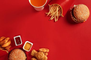 Fast food yemek üstten görünüm. Et burger, patates cipsi ve bardak içki kırmızı zemin üzerine. Paket servisi olan restoran kompozisyon.