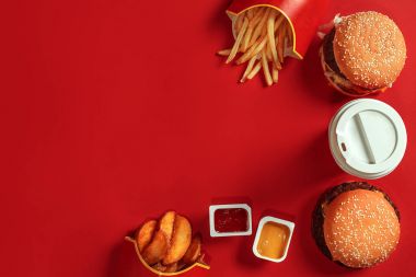 Fast food yemek üstten görünüm. Et burger, patates cipsi ve bardak içki kırmızı zemin üzerine. Paket servisi olan restoran kompozisyon.