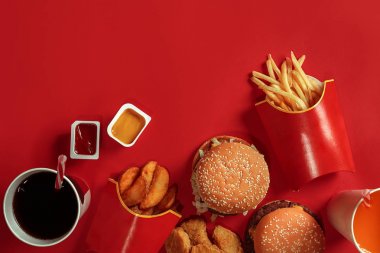 İki hamburger ve patates kızartması, soslar ve içecekler kırmızı zemin üzerine. Fast food. Üstten Görünüm, düz ile boşaltmak yatıyordu