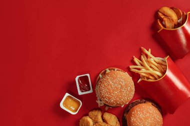 İki hamburger ve patates kızartması, kırmızı zemin üzerine soslar. Fast food. Üstten Görünüm.