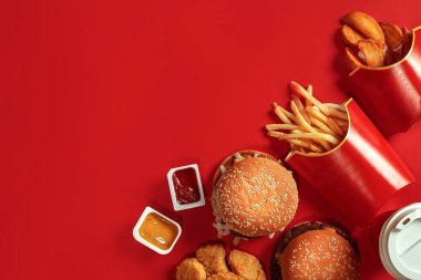 Fast food yemek üstten görünüm. Et burger, patates cipsi ve bardak içki kırmızı zemin üzerine. Paket servisi olan restoran kompozisyon.
