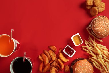 Fast food yemek üstten görünüm. Et burger, patates cipsi ve bardak içki kırmızı zemin üzerine. Paket servisi olan restoran kompozisyon.