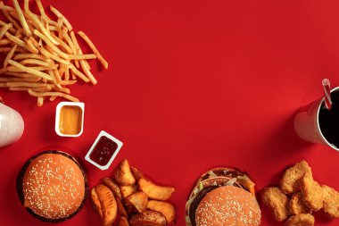 Fast food yemek üstten görünüm. Et burger, patates cipsi ve bardak içki kırmızı zemin üzerine. Paket servisi olan restoran kompozisyon.