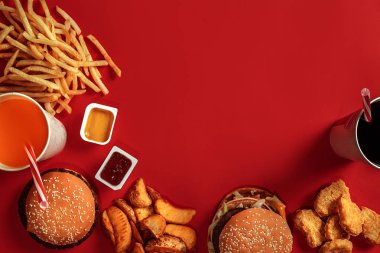 Fast food yemek üstten görünüm. Et burger, patates cipsi ve bardak içki kırmızı zemin üzerine. Paket servisi olan restoran kompozisyon.