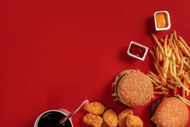 Fast food yemek üstten görünüm. Et burger, patates cipsi ve bardak içki kırmızı zemin üzerine. Paket servisi olan restoran kompozisyon.