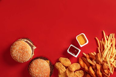 Fast food yemek üstten görünüm. Et burger, patates cipsi ve nuggets kırmızı zemin üzerine. Paket servisi olan restoran kompozisyon.
