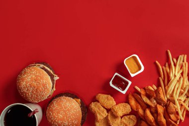 Fast food yemek üstten görünüm. Et burger, patates cipsi ve bardak içki kırmızı zemin üzerine. Paket servisi olan restoran kompozisyon.
