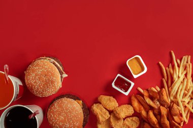 Fast food yemek üstten görünüm. Et burger, patates cipsi ve bardak içki kırmızı zemin üzerine. Paket servisi olan restoran kompozisyon.