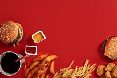 Fast food yemek üstten görünüm. Et burger, patates cipsi ve bardak içki kırmızı zemin üzerine. Paket servisi olan restoran kompozisyon.