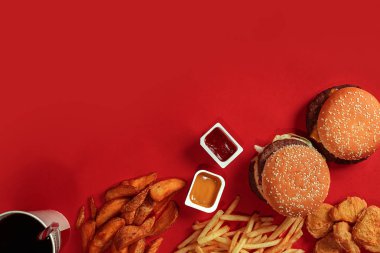 Fast food yemek üstten görünüm. Et burger, patates cipsi ve bardak içki kırmızı zemin üzerine. Paket servisi olan restoran kompozisyon.