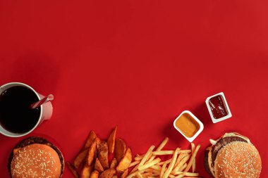 Fast food yemek üstten görünüm. Et burger, patates cipsi ve bardak içki kırmızı zemin üzerine. Paket servisi olan restoran kompozisyon.