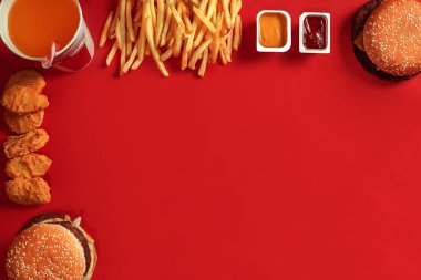 Fast food yemek üstten görünüm. Et burger, patates cipsi ve bardak içki kırmızı zemin üzerine. Paket servisi olan restoran kompozisyon.