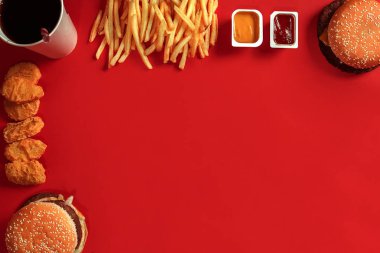 Fast food yemek üstten görünüm. Et burger, patates cipsi ve bardak içki kırmızı zemin üzerine. Paket servisi olan restoran kompozisyon.
