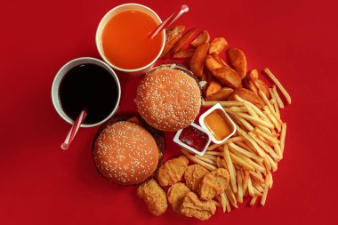 İki hamburger ve patates kızartması, soslar ve içecekler kırmızı zemin üzerine. Fast food. Üstten Görünüm, düz ile boşaltmak yatıyordu