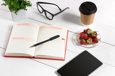 Ofis tablo büro malzemeleri, beyaz boş not defteri, Kupası, kalem, tablet, gözlük, kümesiyle beyaz arka plan üzerinde çiçek. Üstten Görünüm