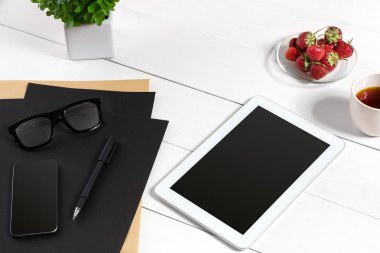 Modern çalışma alanı ile dijital tablet bilgisayar ve cep telefonu, fincan kahve, kalem ve boş kağıt sayfası.