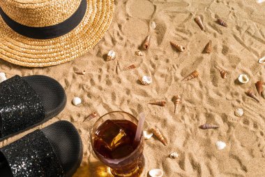 Yaz beachwear, flip flop, şapka, soğuk içecek bir bardak ve kabukları üzerinde kum plaj.