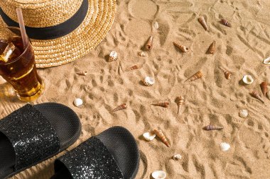 Yaz beachwear, flip flop, şapka, soğuk içecek bir bardak ve kabukları üzerinde kum plaj.