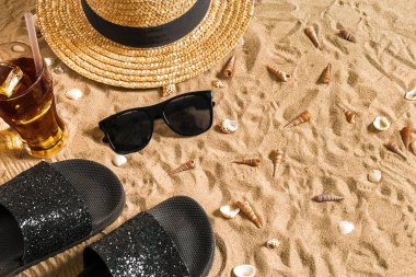 Yaz beachwear, flip flop, şapka, soğuk içecek bir bardak ve kabukları üzerinde kum plaj.