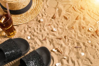 Yaz beachwear, flip flop, şapka, soğuk içecek bir bardak ve kabukları üzerinde kum plaj.