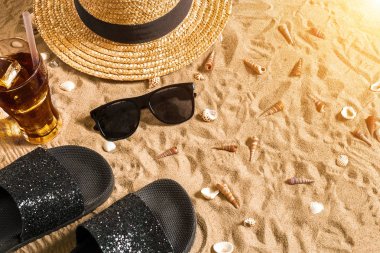 Yaz beachwear, flip flop, şapka, soğuk içecek bir bardak ve kabukları üzerinde kum plaj.
