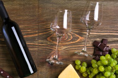 İki bardak, bir şişe kırmızı şarap ve üzüm ahşap bir masa üzerinde