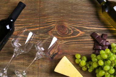 Kırmızı ve beyaz şarap şişeleri, üzüm, peynir ve ahşap masa üzerinde gözlük. Kopya alanı ile Üstten Görünüm