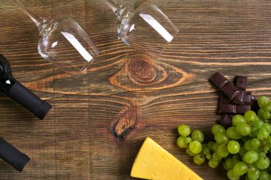 Kırmızı ve beyaz şarap şişeleri, üzüm, peynir ve ahşap masa üzerinde gözlük. Kopya alanı ile Üstten Görünüm