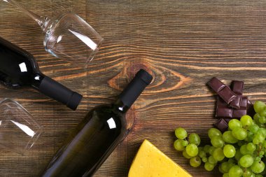 Kırmızı ve beyaz şarap şişeleri, üzüm, peynir ve ahşap masa üzerinde gözlük. Kopya alanı ile Üstten Görünüm