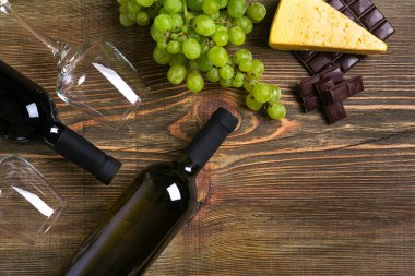 Kırmızı ve beyaz şarap şişeleri, üzüm, peynir ve ahşap masa üzerinde gözlük. Kopya alanı ile Üstten Görünüm