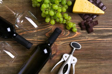 Kırmızı ve beyaz şarap şişeleri, üzüm, peynir ve ahşap masa üzerinde gözlük. Kopya alanı ile Üstten Görünüm