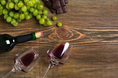 İki bardak, bir şişe kırmızı şarap ve üzüm ahşap bir masa üzerinde