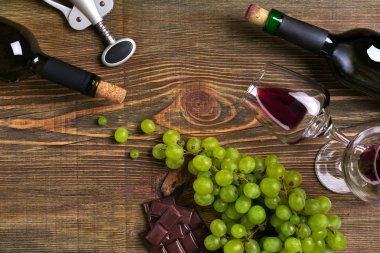 Kırmızı ve beyaz şarap şişeleri, üzüm, çikolata ve ahşap masa üzerinde gözlük. Kopya alanı ile Üstten Görünüm